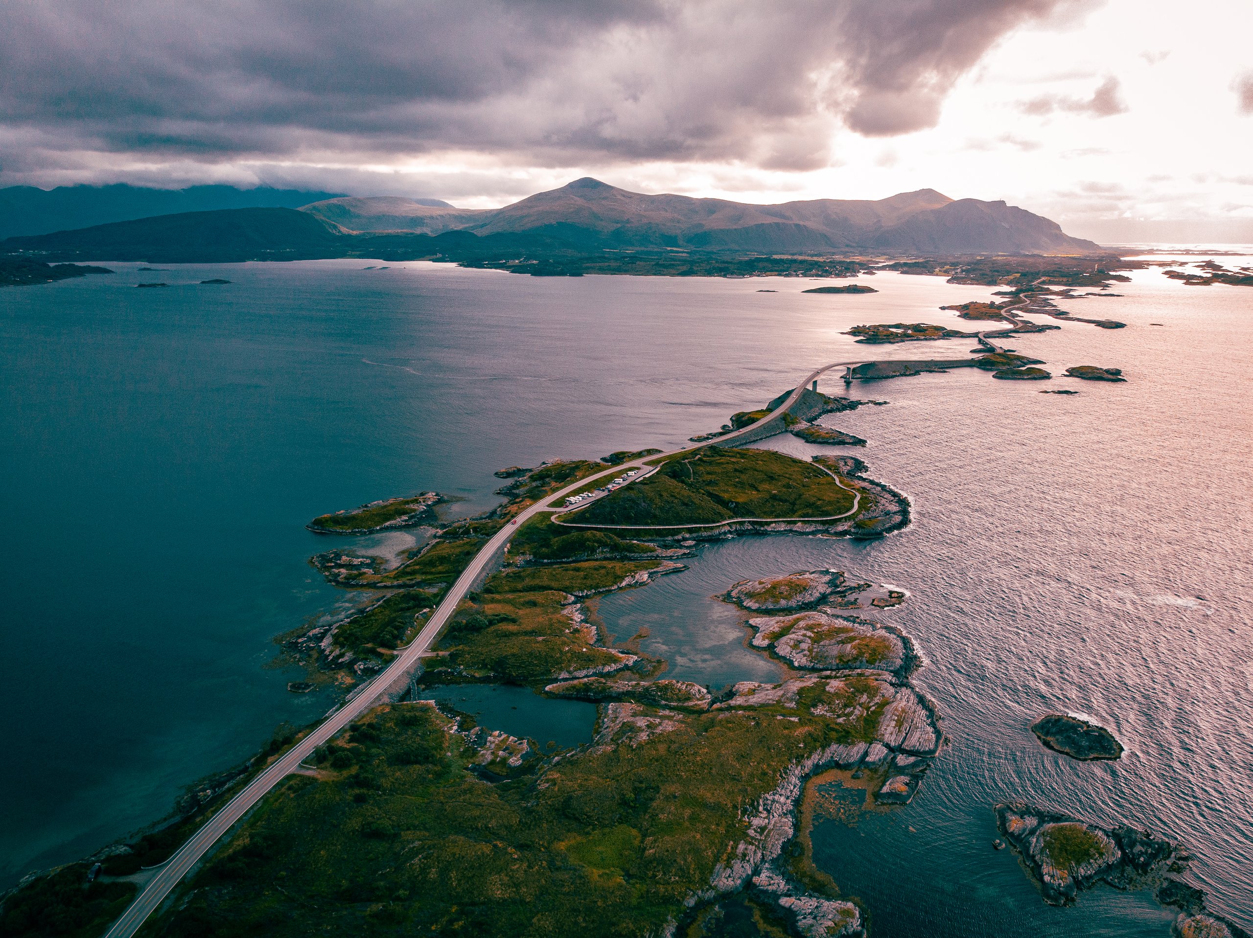 Aerial view from directly above of a winding coastal road crossing small islands, with the sea and mountains all around